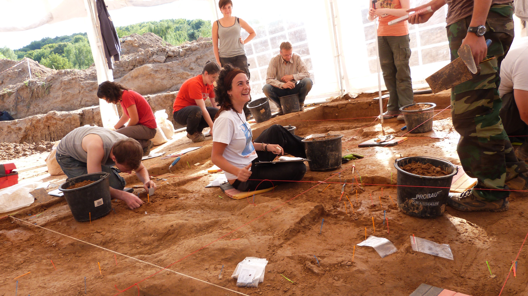 The photo shows an excavation site with eight people working.