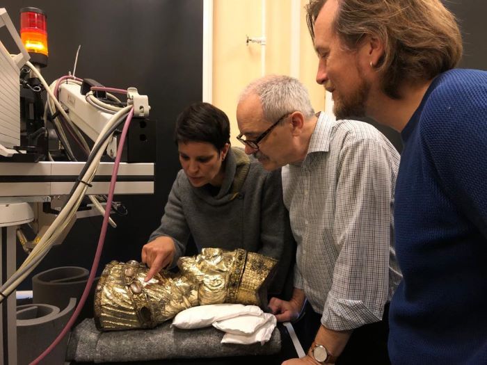 A woman and two men stand around a shiny gold sculpture and examine it.