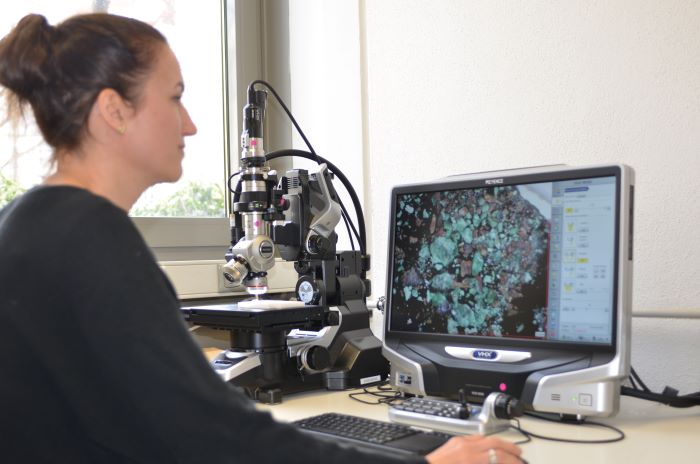 Employee in front of a screen with a digital microscope in the background.