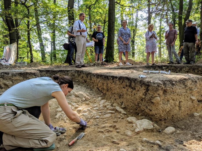 People in the background of an excavation, in front an employee examines the excavation site.