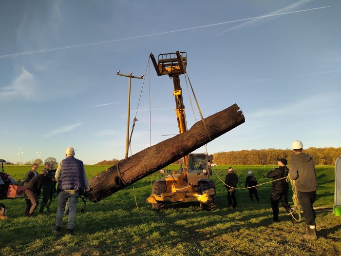 Bergung eines mittelalterlichen Bootswracks durch einen Kran. Zwei Personen stehen links und rechts am Rande.