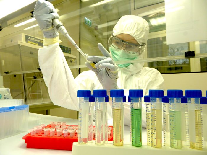 A person in white protective clothing, goggles and a mask takes a sample with a pipette in a laboratory.